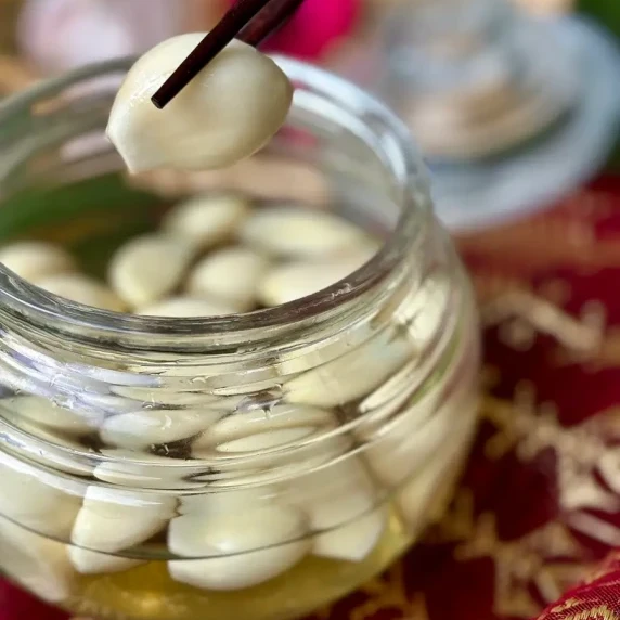Pickled garlic in a glass jar with chopsticks lifting a single clove.