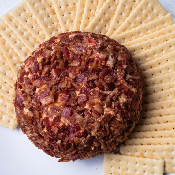Bacon covered cheese ball on a platter with club crackers.