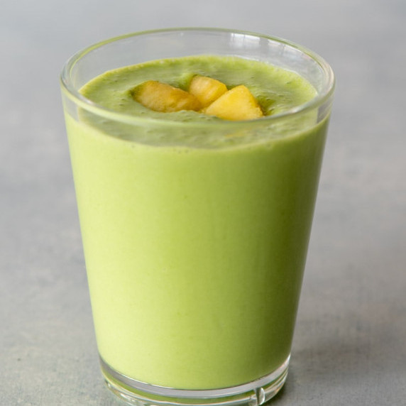 A green smoothie in a tall glass with pineapple pieces garnishing the top.