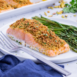 Pistachio-Crusted Salmon RECIPE served on a white plate with asparagus and a fork.