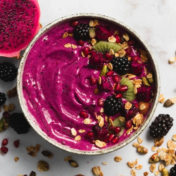 Pitaya Smoothie Bowl arranged in a bowl with topping and berries and dragon fruit on the side
