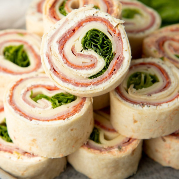 Italian pinwheel roll-ups stacked on a platter, the top pinwheel angled to show the swirls inside.