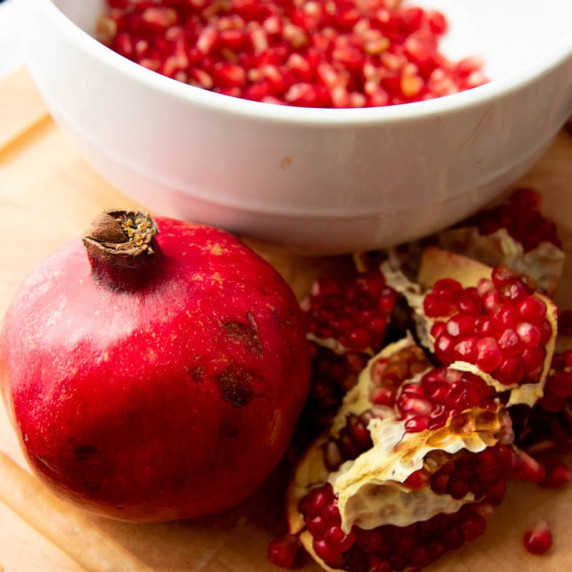 A whole pomegranate and pomegranate sections sit in front of a bowl of pomegranate arils.