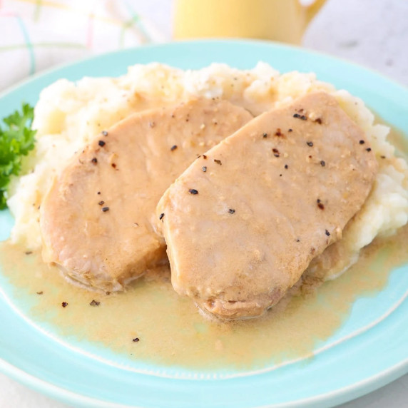 Two pork chops with gravy and salt & pepper served alongside creamy mashed potatoes on a blue plate