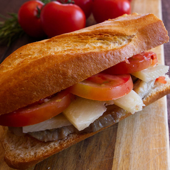 a pork lion sandwich sits with some fresh tomato and cheese