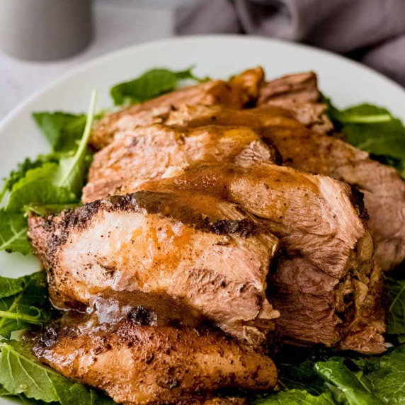 Sliced pork roast with gravy over top, plated on a bed of greens.