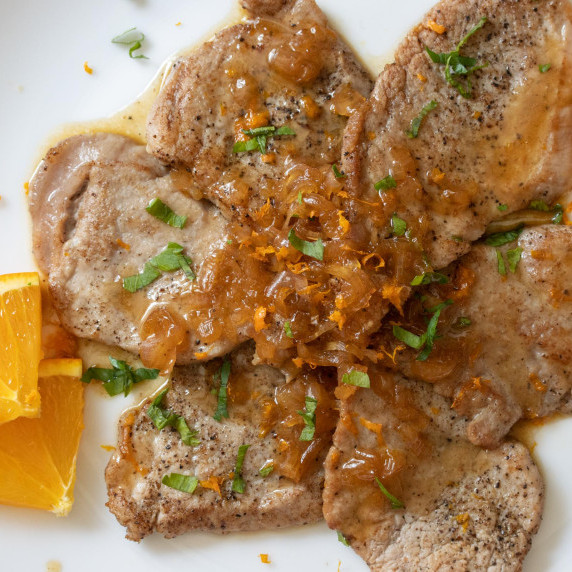 pork tenderloin scaloppini placed in a circular pattern on a white plate with sauce placed over it