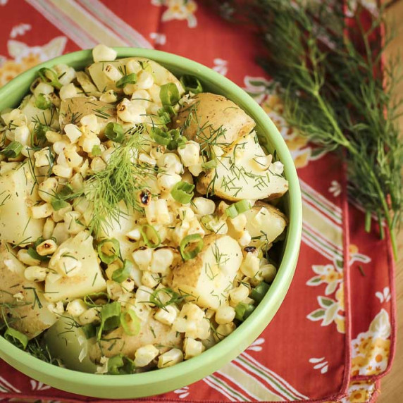 Overhead shot of potato salad with corn garnished with dill and green onions in a green bowl.