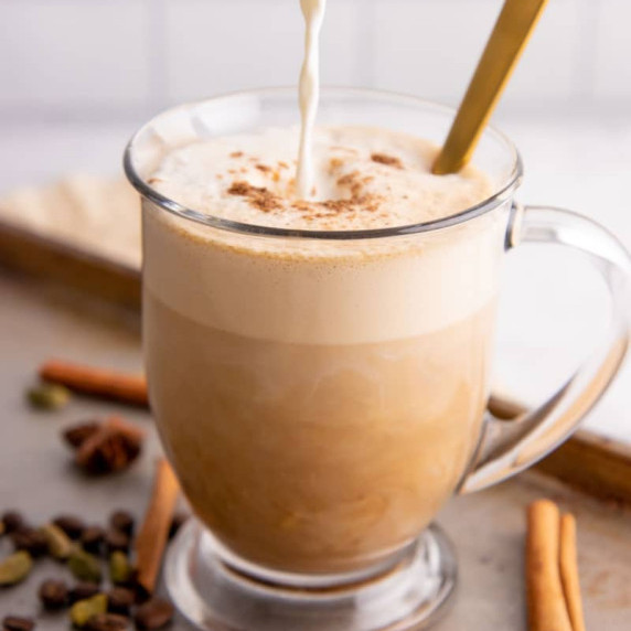 Pouring warm, frothy half-and-half into a mug of chai and espresso to make a dirty chai latte.