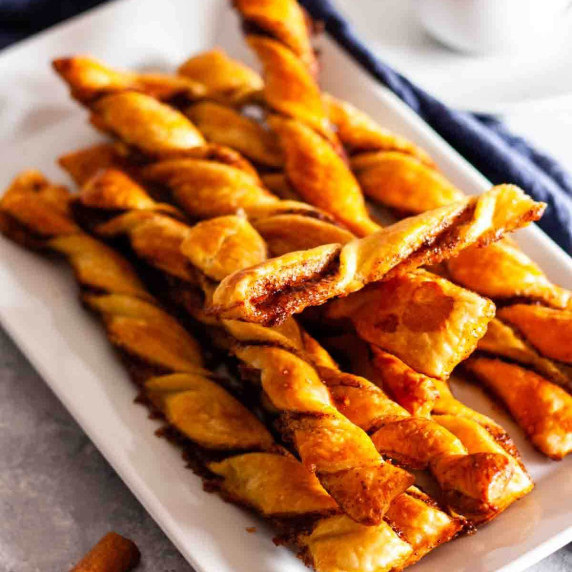 Puff pastry cinnamon twists on a white plate next to a cup of coffee.