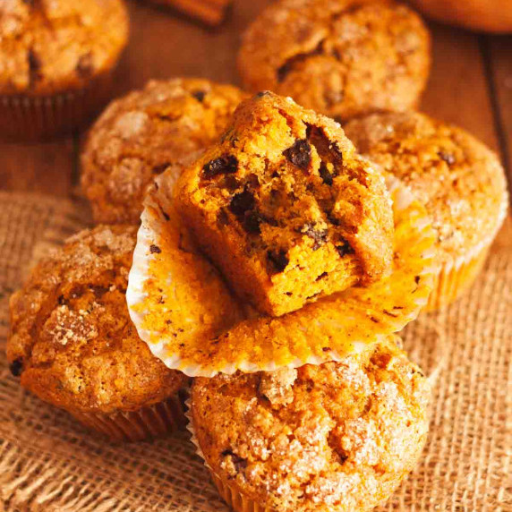 A close up of a bitten pumpkin banana muffin on top of other muffins on burlap.