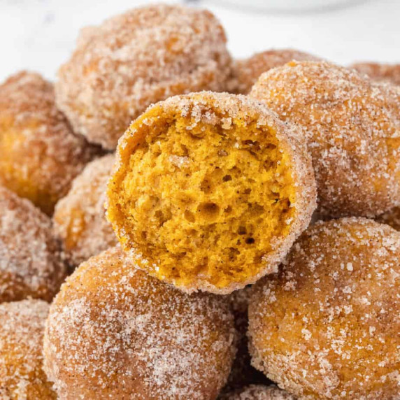 Close up of a pumpkin donut hole missing a bite from the side on top of other donut holes stacked.