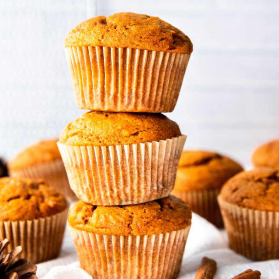 Three fluffy pumpkin muffins stacked on atop the other with more muffins around them.