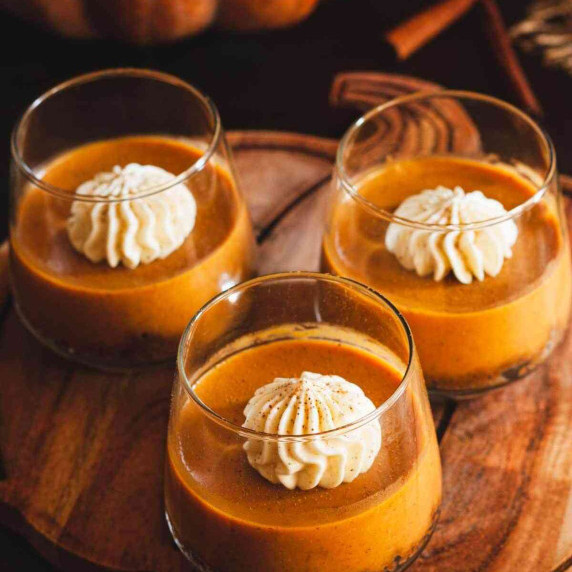 Three pumpkin pie cups on a wooden board in the shape of a pumpkin next to a pumpkin.