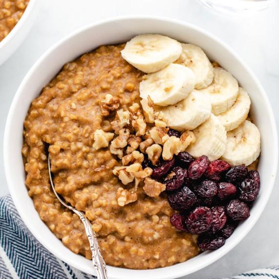 Pumpkin oatmeal in a bowl with dried cranberries, sliced bananas, and walnuts.