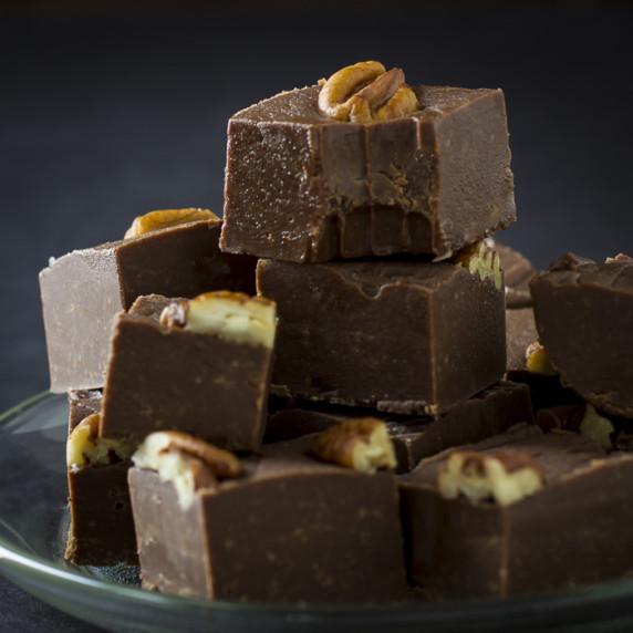 Side close up shot of multiple pieces of fudge stacked on each other on a clear plate.