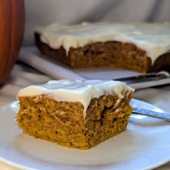 A slice of pumpkin spice cake with cream cheese icing on a plate.