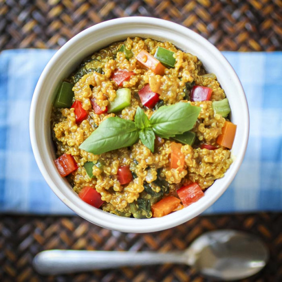 Overhead shot of quinoa curry garnished with fresh herbs in a white bowl on a blue plaid cloth.