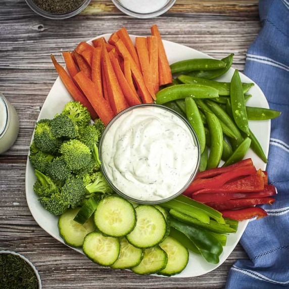 Overhead shot of a white platter with veggies surrounding a clear bowl with homemade ranch dressing 