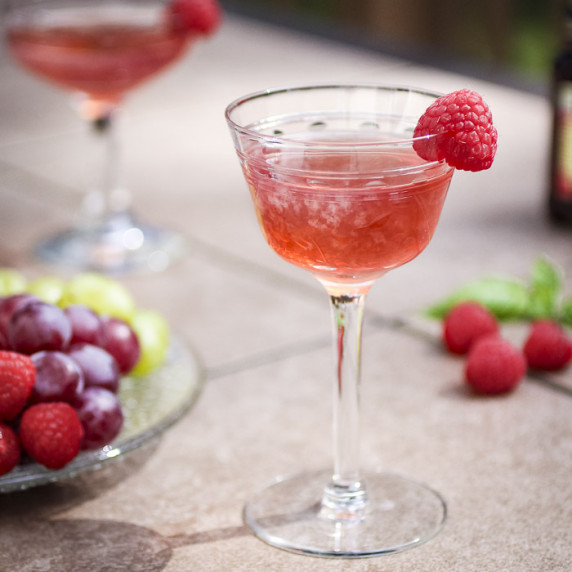 Side shot of a cocktail glass with raspberry gimlet and a raspberry as a garnish.