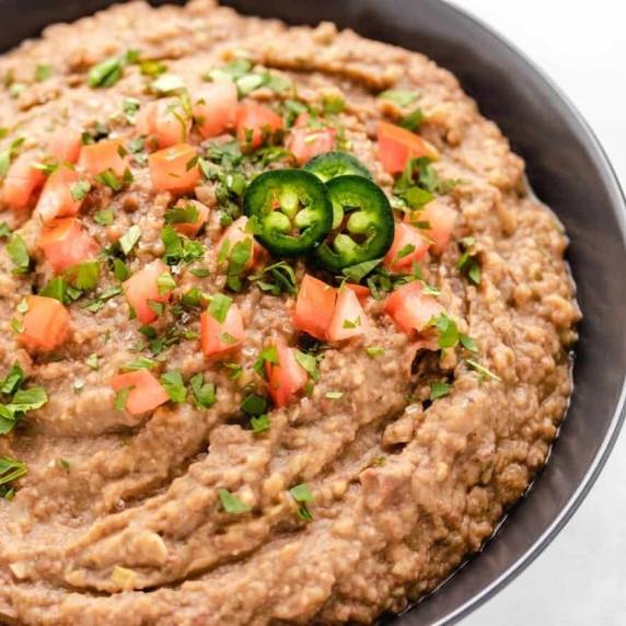 Refried beans in a bowl with diced tomatoes.