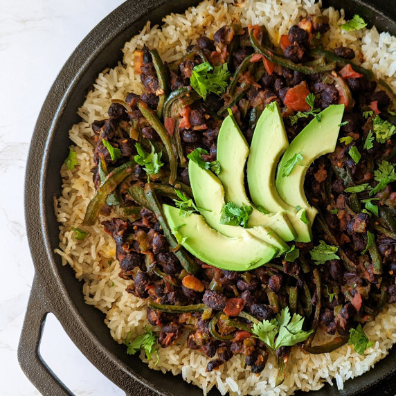 A cast iron skillet with rice, black beans, and veggies topped with avocado slices