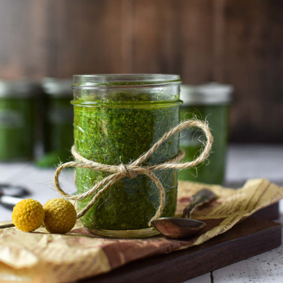 Clear jar of pesto sauce on a wood surface.
