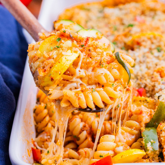 Roasted Vegetable Pasta Bake RECIPE in a white casserole dish with a spoon scooping out a portion.