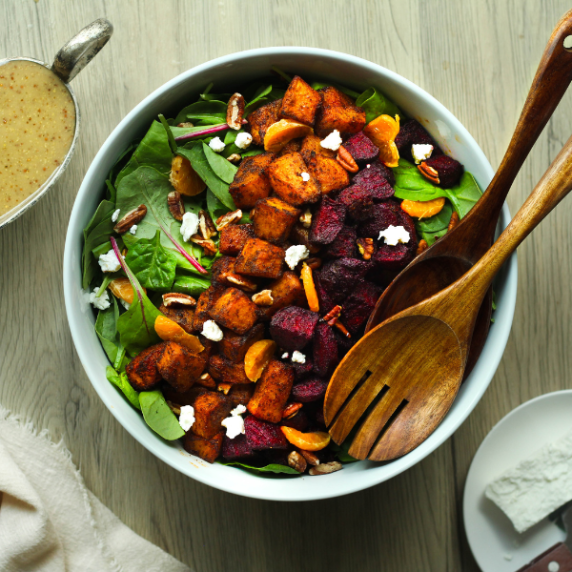 Roasted beetroot and pumpkin salad in a white bowl with wooden spoons.