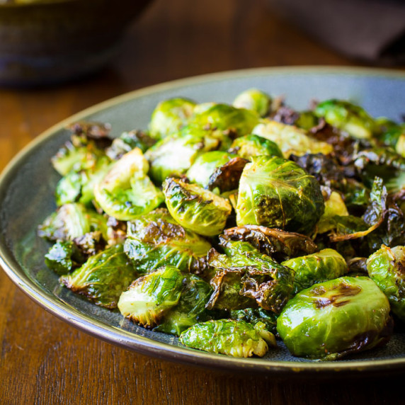 Side shot of garlic roasted Brussel sprouts on a blue and grey plate on a wooden table.