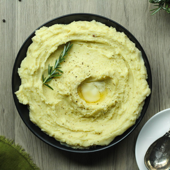 Rosemary garlic mashed potatoes perfect for fall potluck dishes in a black bowl with melting butter.