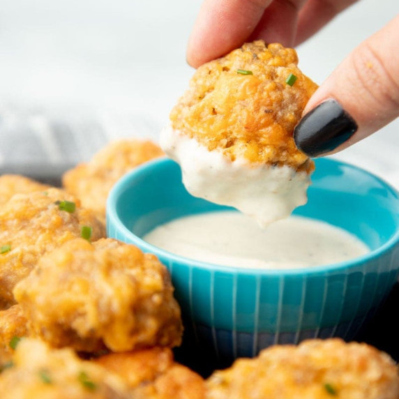Fingers dip a sausage ball in ranch dressing on an appetizer platter heaped high with sausage balls.