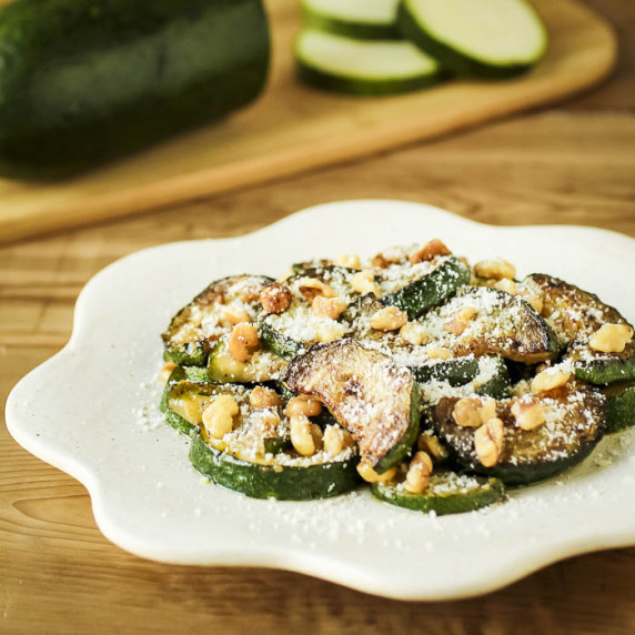Side shot of sauteed zucchini and walnuts with parmesan cheese on a white decorative plate.
