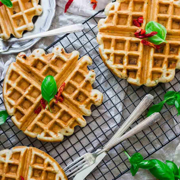 Waffles on a wire rack with basil and red pepper flakes, fork and knife.