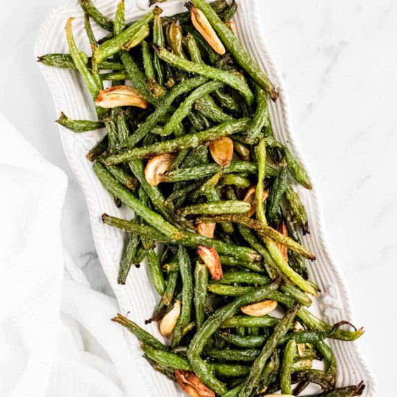 Grilled green beans and garlic cloves piled on a long, white, rectangular serving platter.