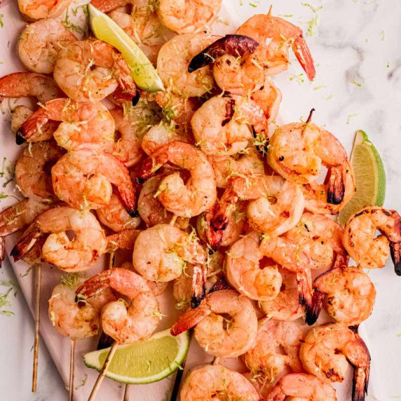 Grilled shrimp skewers arranged on a platter and garnished with lime wedges and zest.