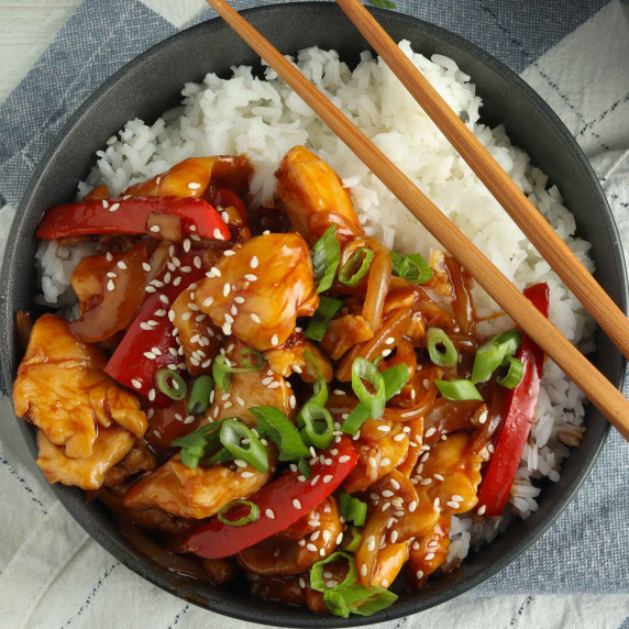 sesame chicken in a bowl on top of rice with chopsticks