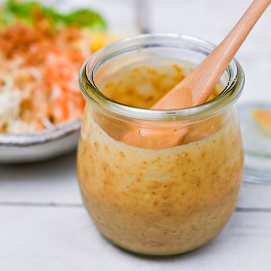 Japanese sesame dressing in a small jar with wooden spoon on a light background