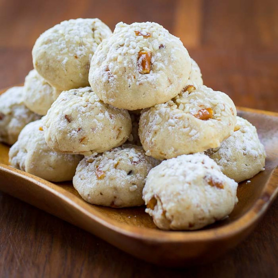 Side view of multiple sesame cookies stacked on a wooden bowl-plate garnished with powdered sugar.