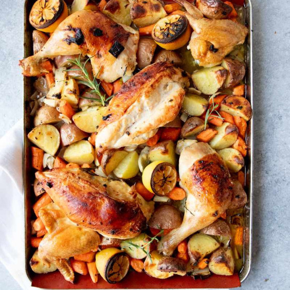 Overhead of a silicone mat lined sheet pan filled with roasted root veggies and chicken pieces.