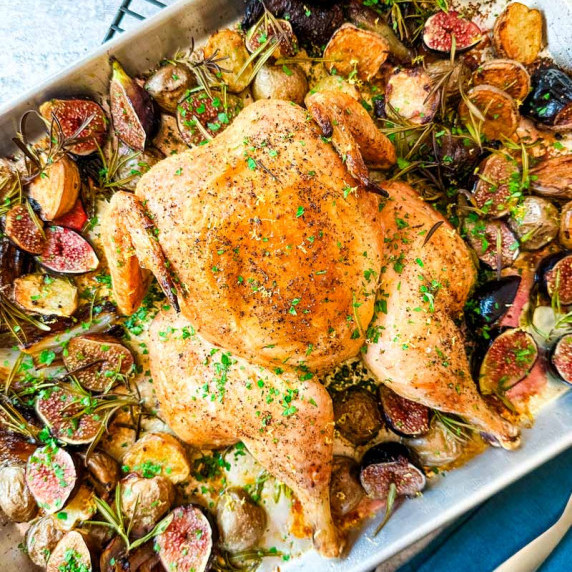 A whole roasted chicken with potatoes and figs on a sheet pan.