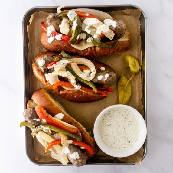 sausage peppers and onions sandwiches on a baking sheet with garlic aioli on top.
