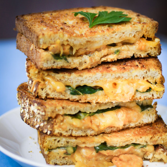 Close up side view of four halves of grilled cheese stacked on each other garnished with herbs.