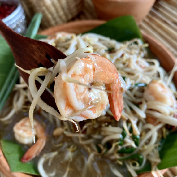A wooden fork with a shrimp and bean sprouts on it. Underneath it is a dish shrimp bean sprouts.