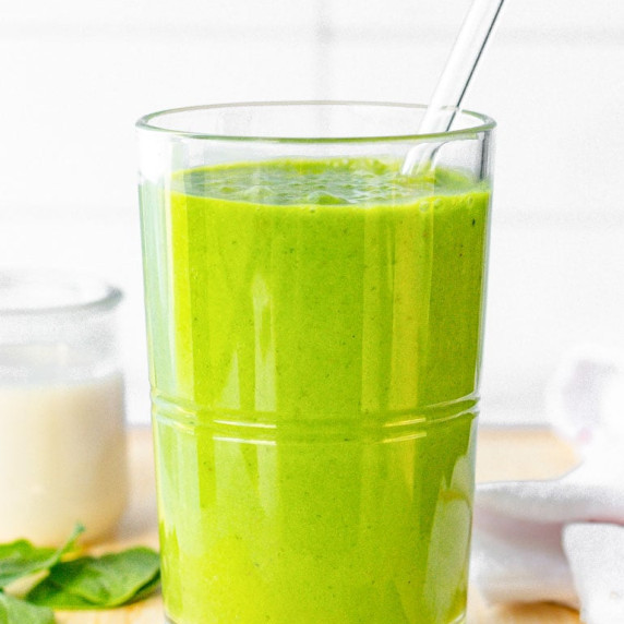 Close-up of a creamy green smoothie in a glass with a glass straw.