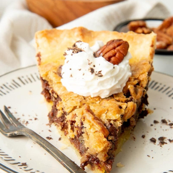 A slice of chocolate bourbon pecan pie sits on a plate garnished with whipped cream.