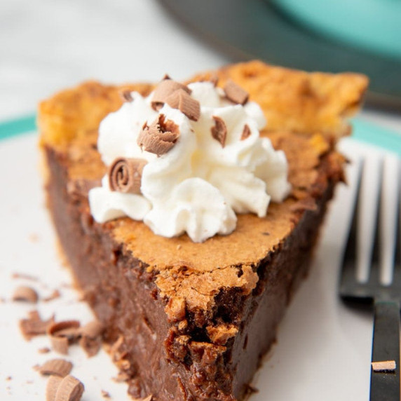 A single slice of chocolate chess pie garnished with whipped cream and chocolate shavings.