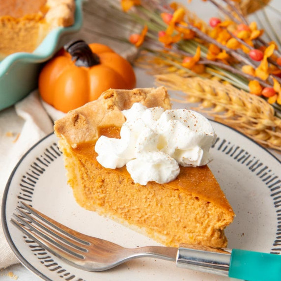 A perfect slice of pumpkin pie topped with whipped cream sits on a plate with a fork beside it.