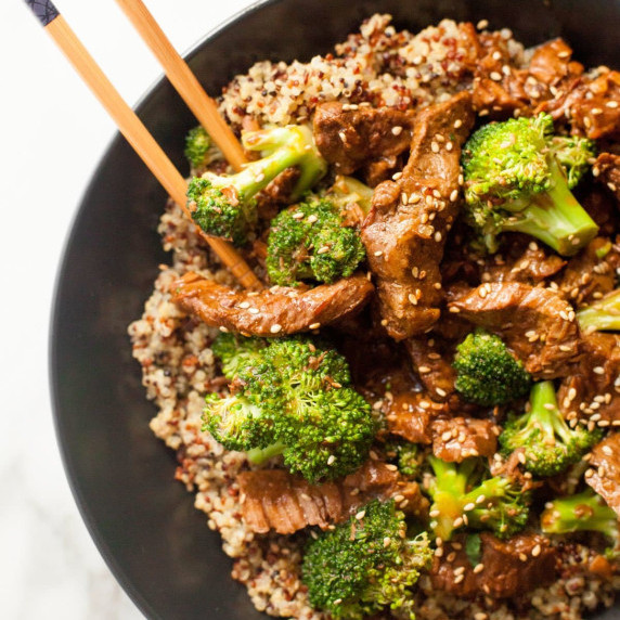 Close view of two chopsticks scooping into a bowl of slow cooker beef and broccoli with quinoa.