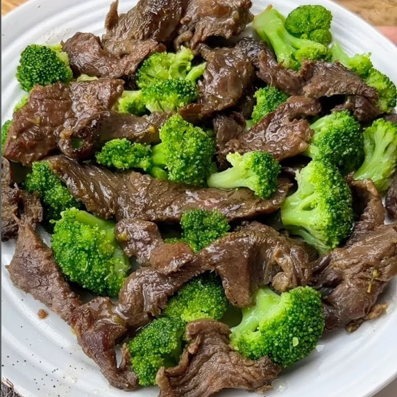 A dish of succulent beef pieces mixed with vibrant green broccoli florets, presented on a white plat